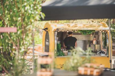 Un food truck jaune dans un cadre extérieur verdoyant, avec une personne préparant des plats à l'intérieur.