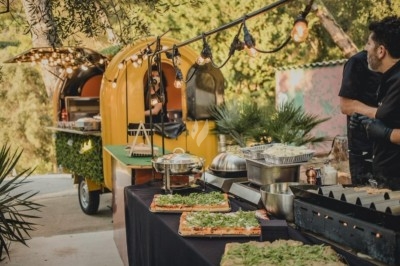 Camion-restaurant jaune décoré de plantes et guirlandes lumineuses, proposant pâtes, gnocchis et cocktails.