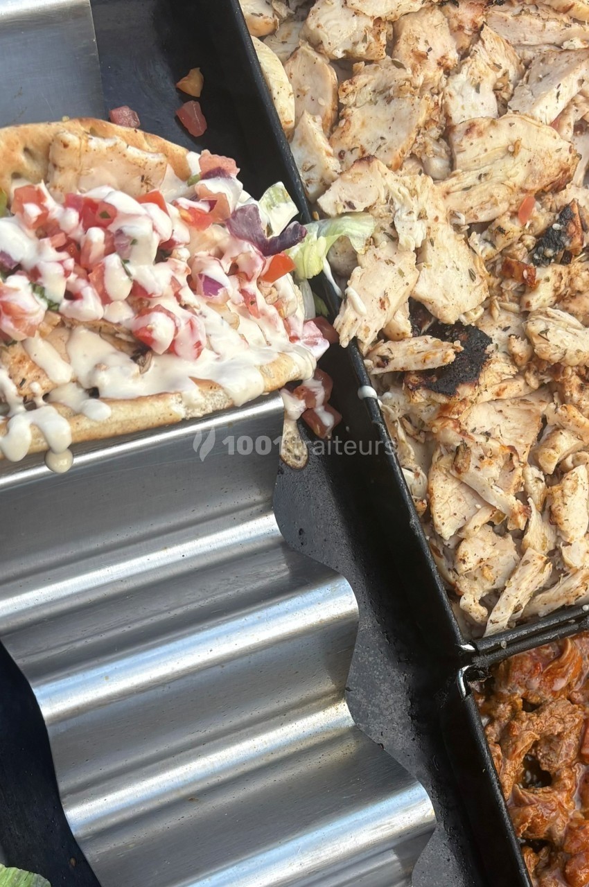 Viande grillée, pain garni de légumes et sauce blanche, disposés sur un présentoir en métal et un plateau.
