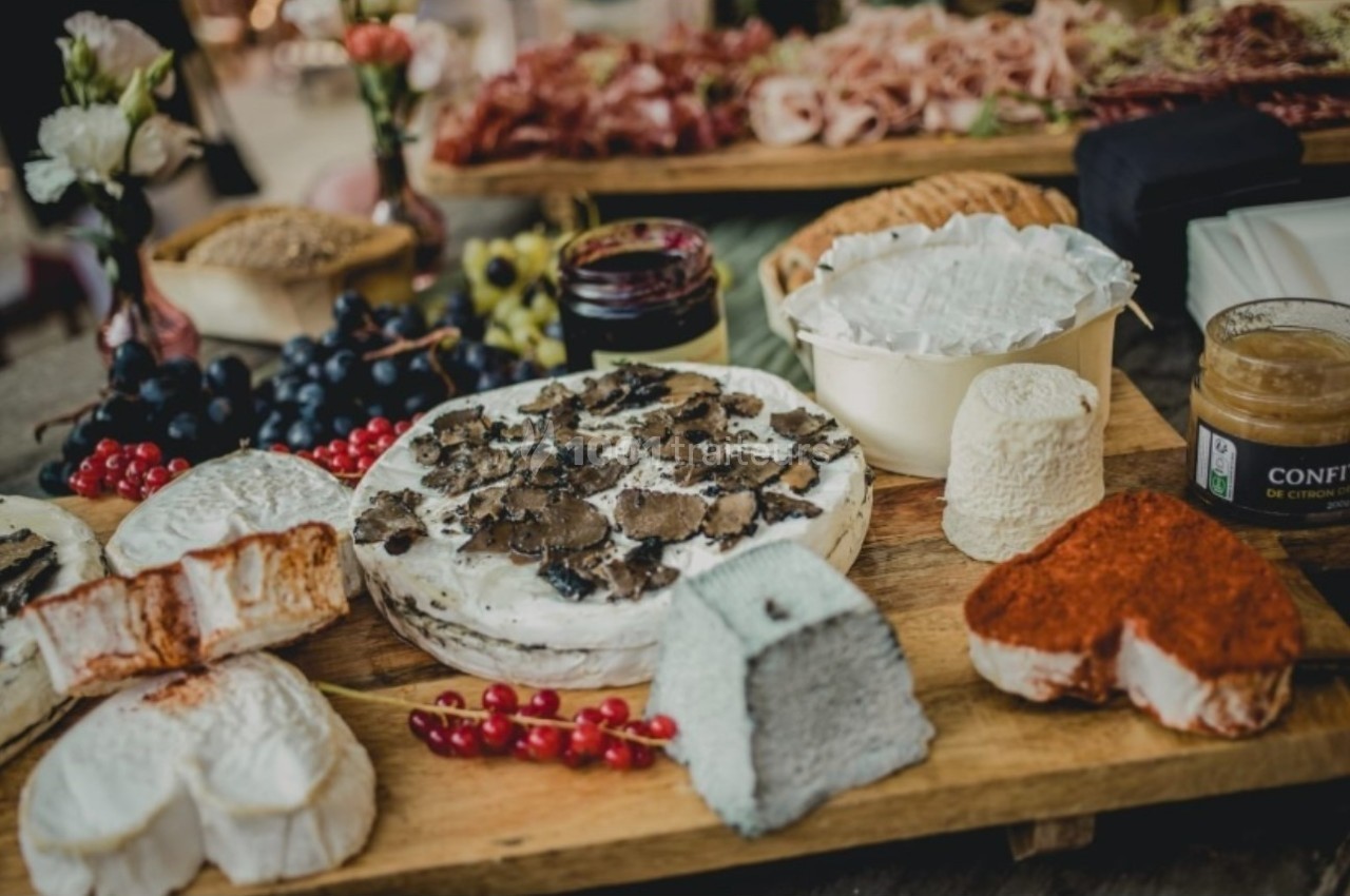 Plateau de fromages variés avec truffes, fruits rouges, raisins et confiture, présenté sur une table en bois.