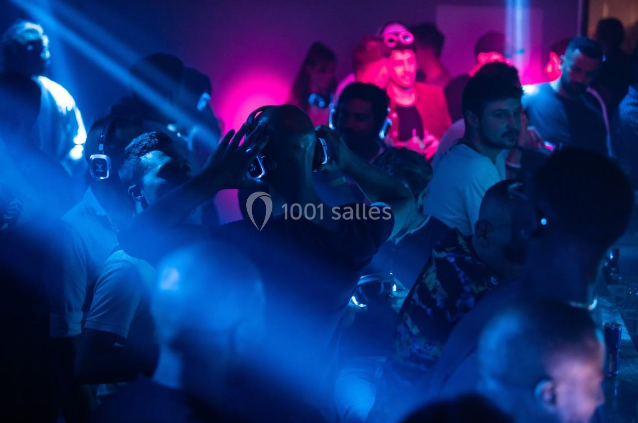 Personnes dansant avec des casques audio dans une ambiance de lumière bleue et rose lors d'une soirée silencieuse.