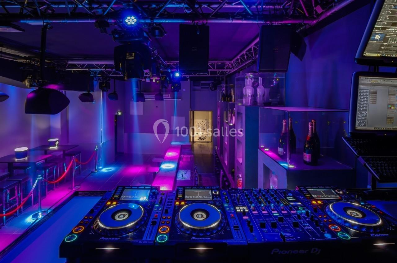 Console de DJ avec platines et éclairage coloré dans une salle de club vide.