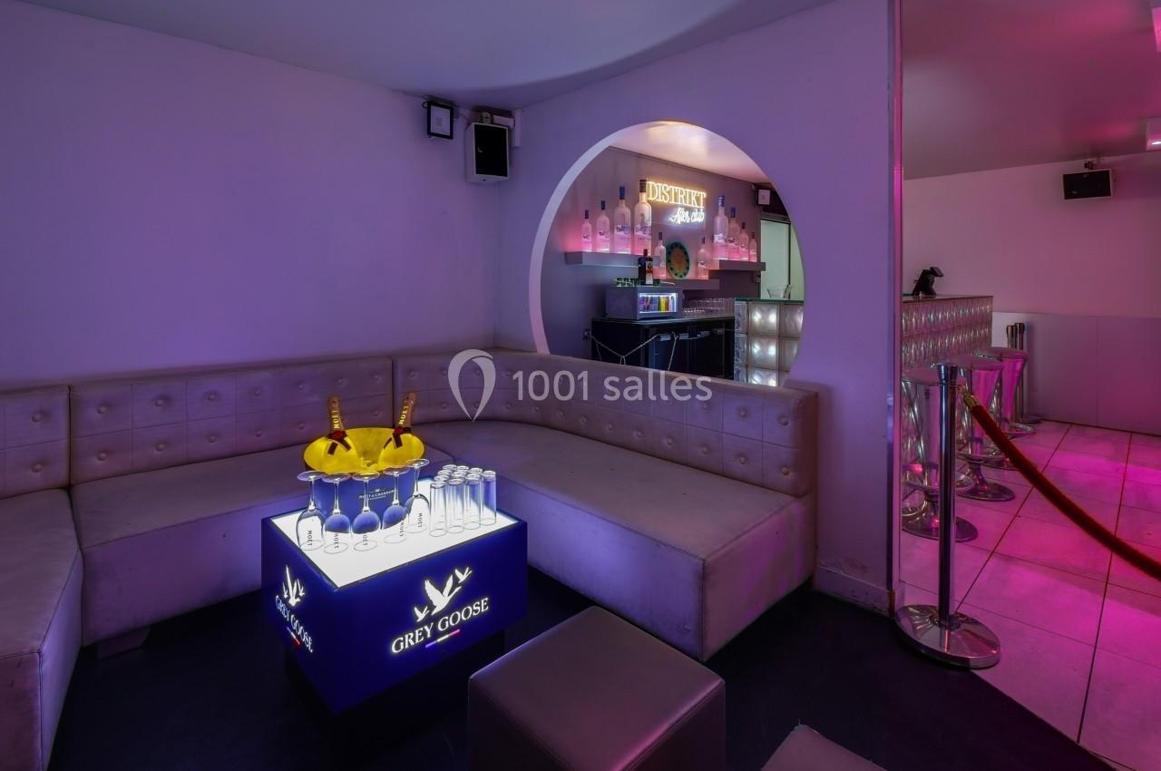 Banquette en cuir beige dans un lounge avec table lumineuse, seaux à champagne et bar éclairé en arrière-plan.