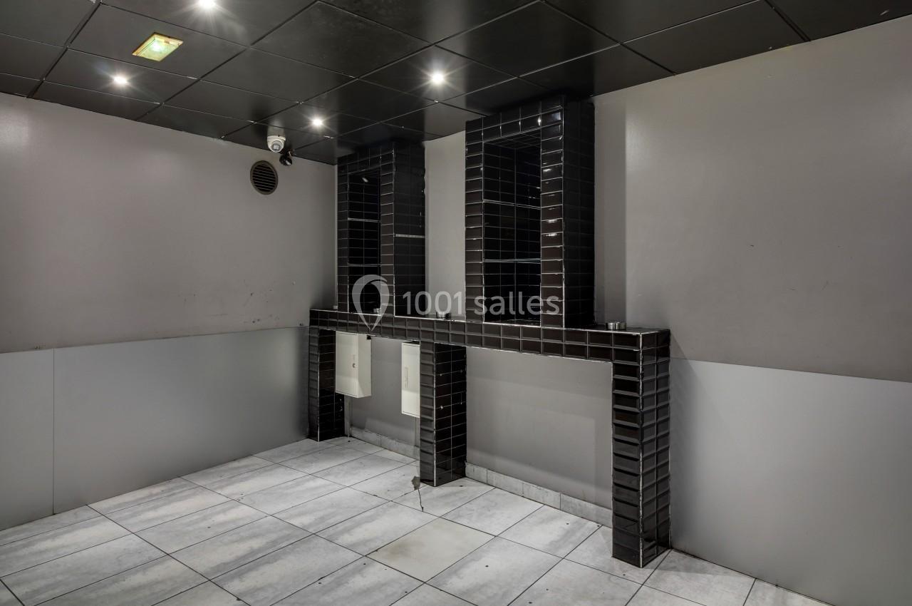 Salle de bain moderne avec murs gris, carrelage au sol clair, et lavabos intégrés dans un meuble noir carrelé.