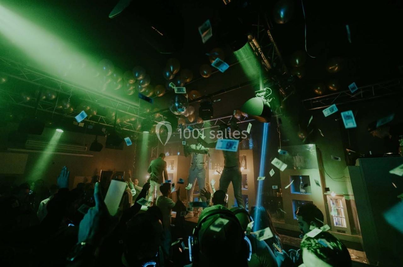 Des personnes dans une salle sombre avec des lumières colorées, des billets en l'air et des ballons suspendus au plafond.