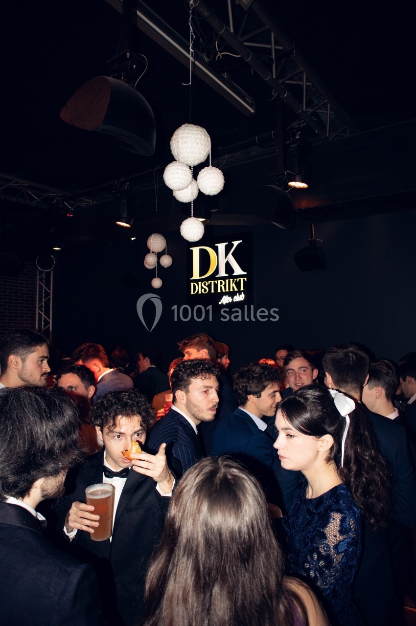 Groupe de personnes en tenue de soirée dans un club sombre avec un panneau ’DK Distrikt’ illuminé en arrière-plan.