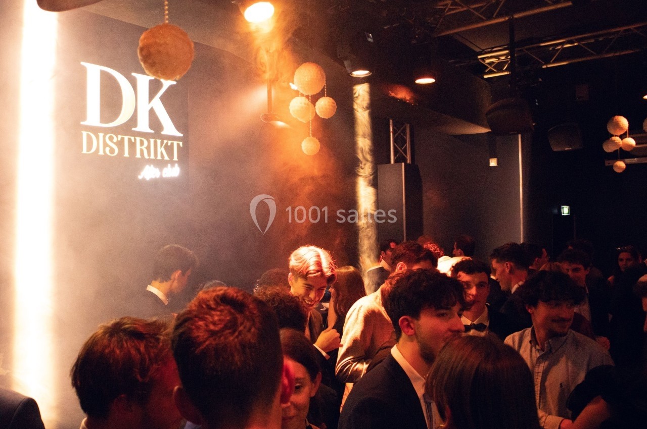 Foule de personnes dans un club nocturne avec des lumières tamisées et le logo ’DK Distrikt’ visible sur un mur.
