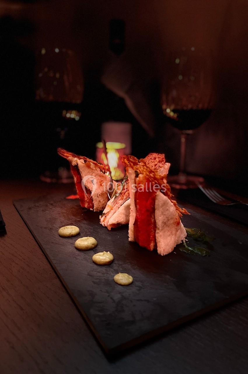 Assiette gastronomique avec des bouchées élégantes sur ardoise, accompagnées de sauce en points, dans une ambiance tamisée.