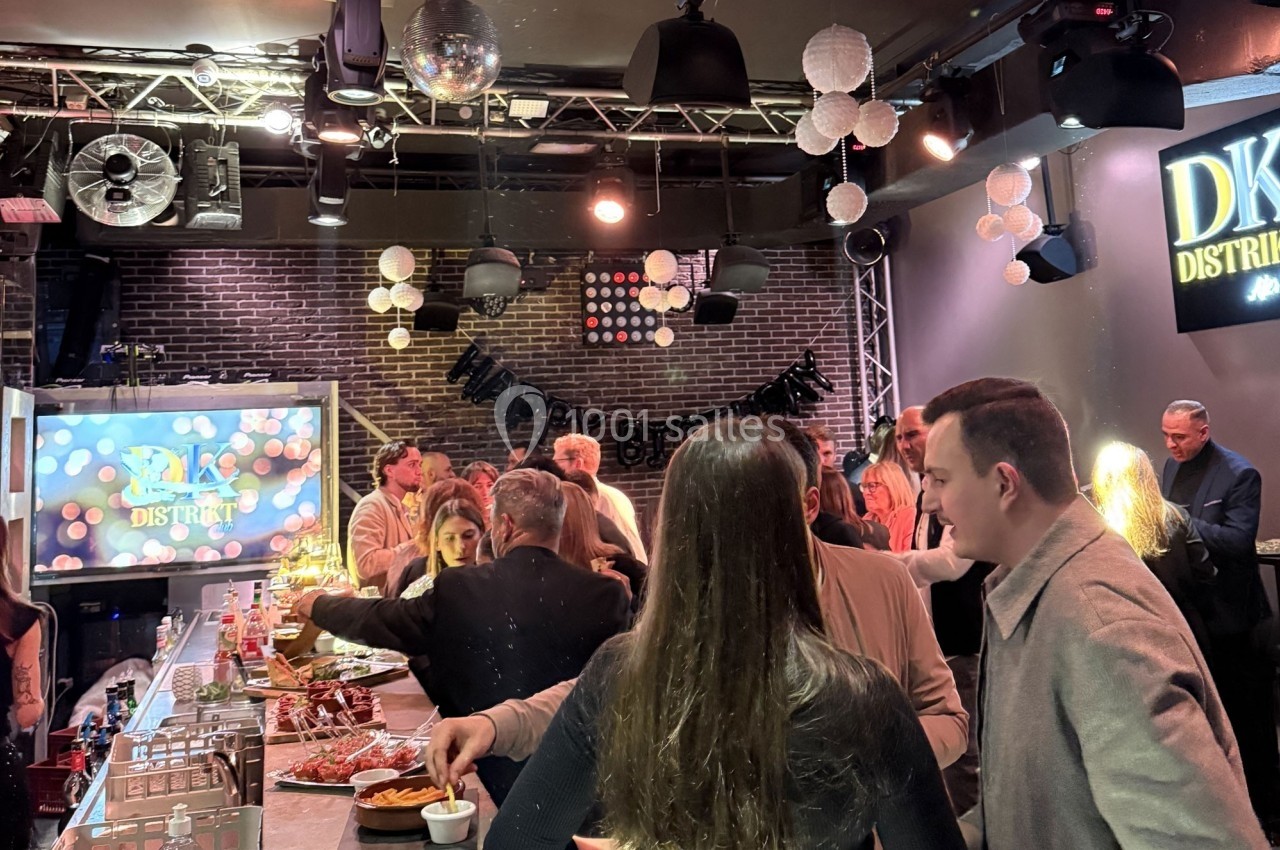 Des personnes rassemblées dans un bar ou restaurant, discutant et se servant à un buffet sous une décoration lumineuse.
