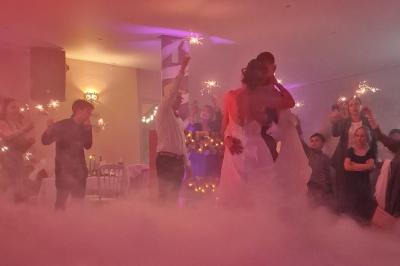 Un couple danse sur une piste extérieure éclairée, entouré de bulles, avec un DJ en arrière-plan.