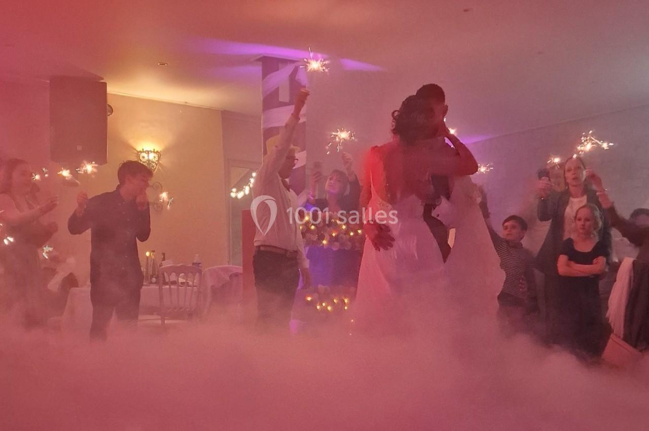 Un couple danse dans une salle éclairée de lumières tamisées, entouré d'invités tenant des cierges magiques.