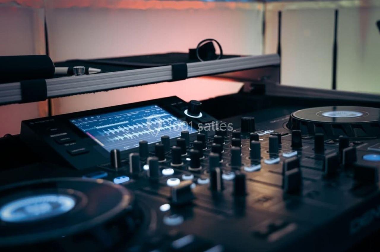 Table de mixage avec platines et écran affichant des ondes sonores, éclairée par une lumière tamisée.