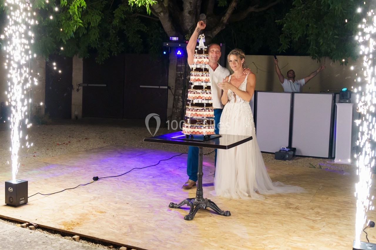 Un couple en tenue de mariage coupe une pièce montée sous des étincelles, en extérieur, de nuit.