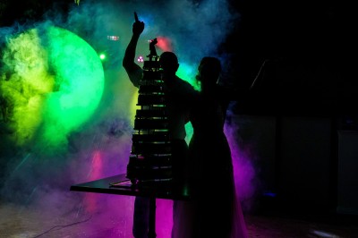 Un couple danse sur une piste extérieure éclairée, entouré de bulles, avec un DJ en arrière-plan.