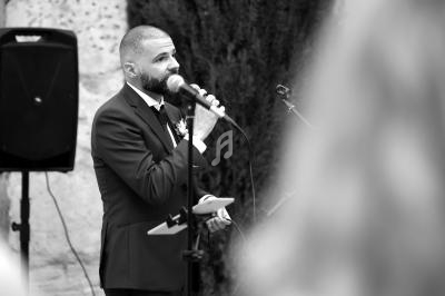 Un homme en costume parle dans un micro lors d'un événement en extérieur, tenant des notes en main.