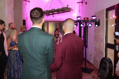 Deux hommes en costume, vus de dos, assistent à un événement dans une salle éclairée par des lumières roses.