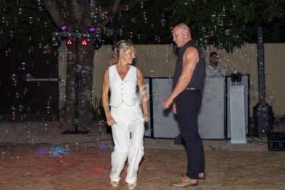 Un couple danse sur une piste extérieure éclairée, entouré de bulles, avec un DJ en arrière-plan.