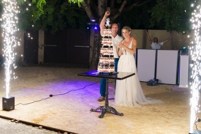 Un couple en tenue de mariage coupe une pièce montée sous des étincelles, en extérieur, de nuit.