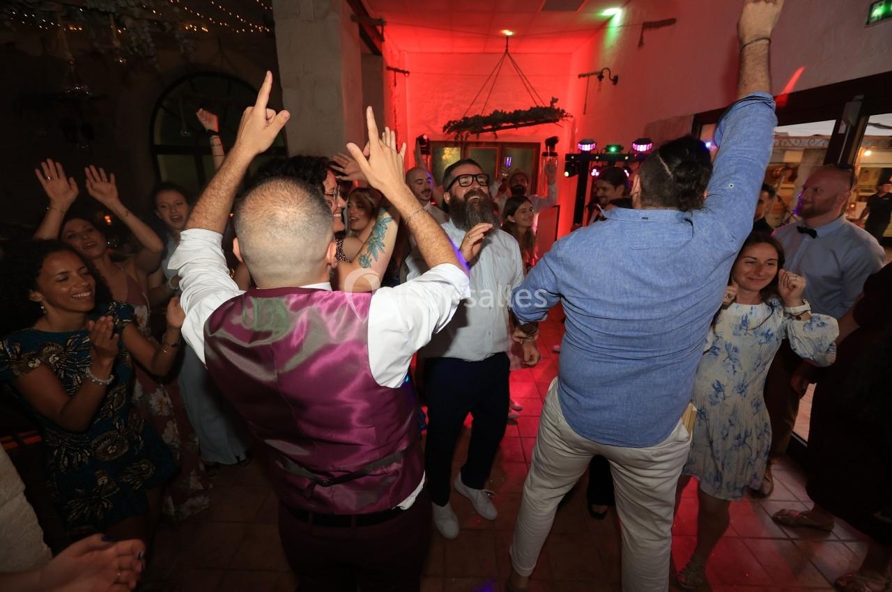 Des personnes dansent et célèbrent dans une salle éclairée, avec des lumières colorées et une ambiance festive.