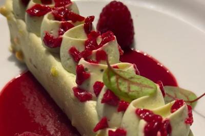 Dessert raffiné composé d'une mousse blanche garnie de morceaux de framboise, sur un coulis rouge, décoré d'une feuille…