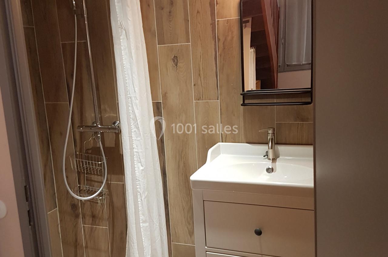 Salle de bain avec douche à l'italienne, carrelage effet bois, meuble blanc avec lavabo et miroir éclairé.