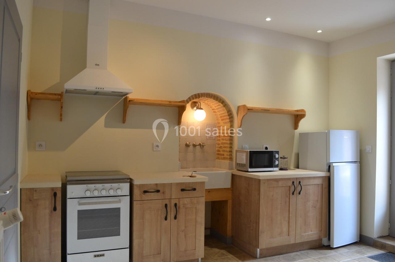 Cuisine équipée avec meubles en bois, évier, cuisinière, hotte, micro-ondes, réfrigérateur et éclairage mural.