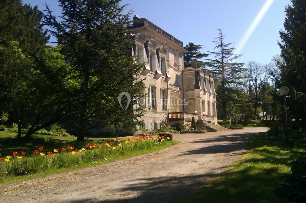 Manoir ancien entouré d'un jardin fleuri avec des tulipes, bordé d'arbres et baigné de lumière naturelle.
