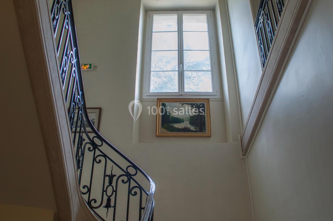 Escalier intérieur en pierre avec rampe en fer forgé, éclairé par une fenêtre laissant entrer la lumière naturelle.