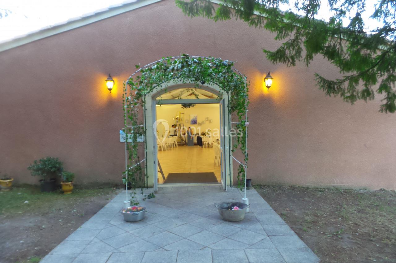 Entrée d'un bâtiment décorée de feuillage et de lumières, donnant sur une salle lumineuse avec des tables et des chaises.