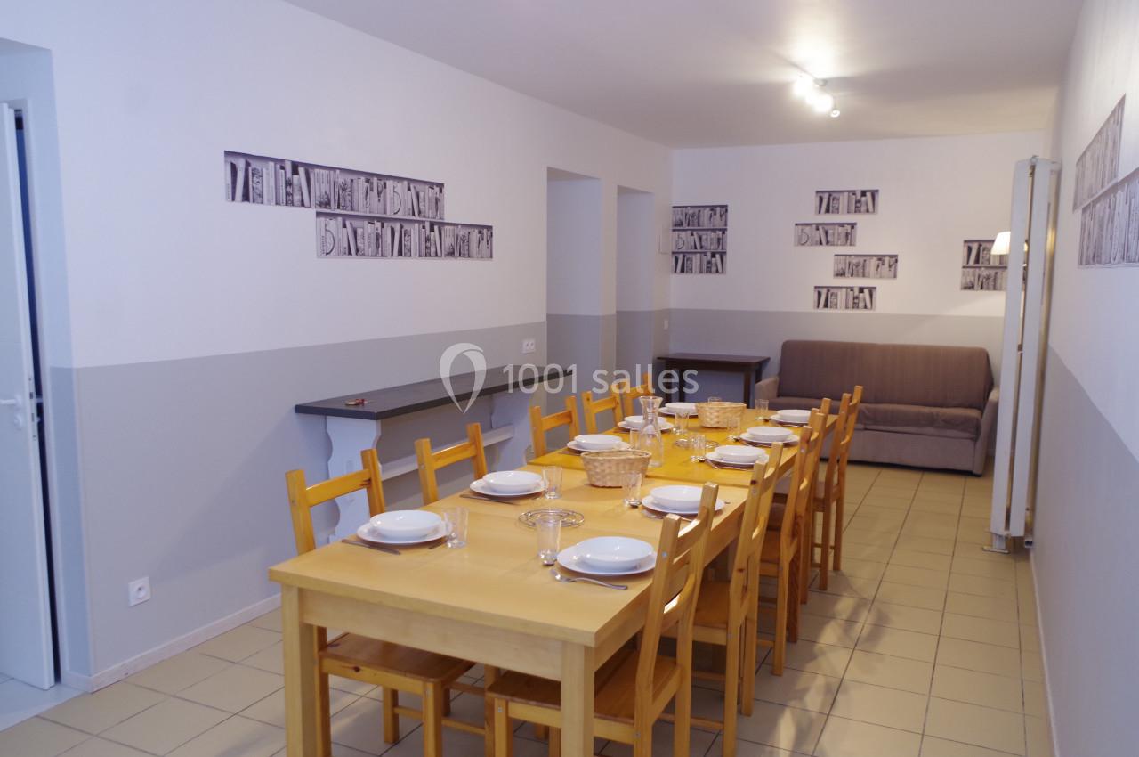 Salle à manger avec une grande table en bois, chaises assorties, vaisselle disposée et un canapé en arrière-plan.