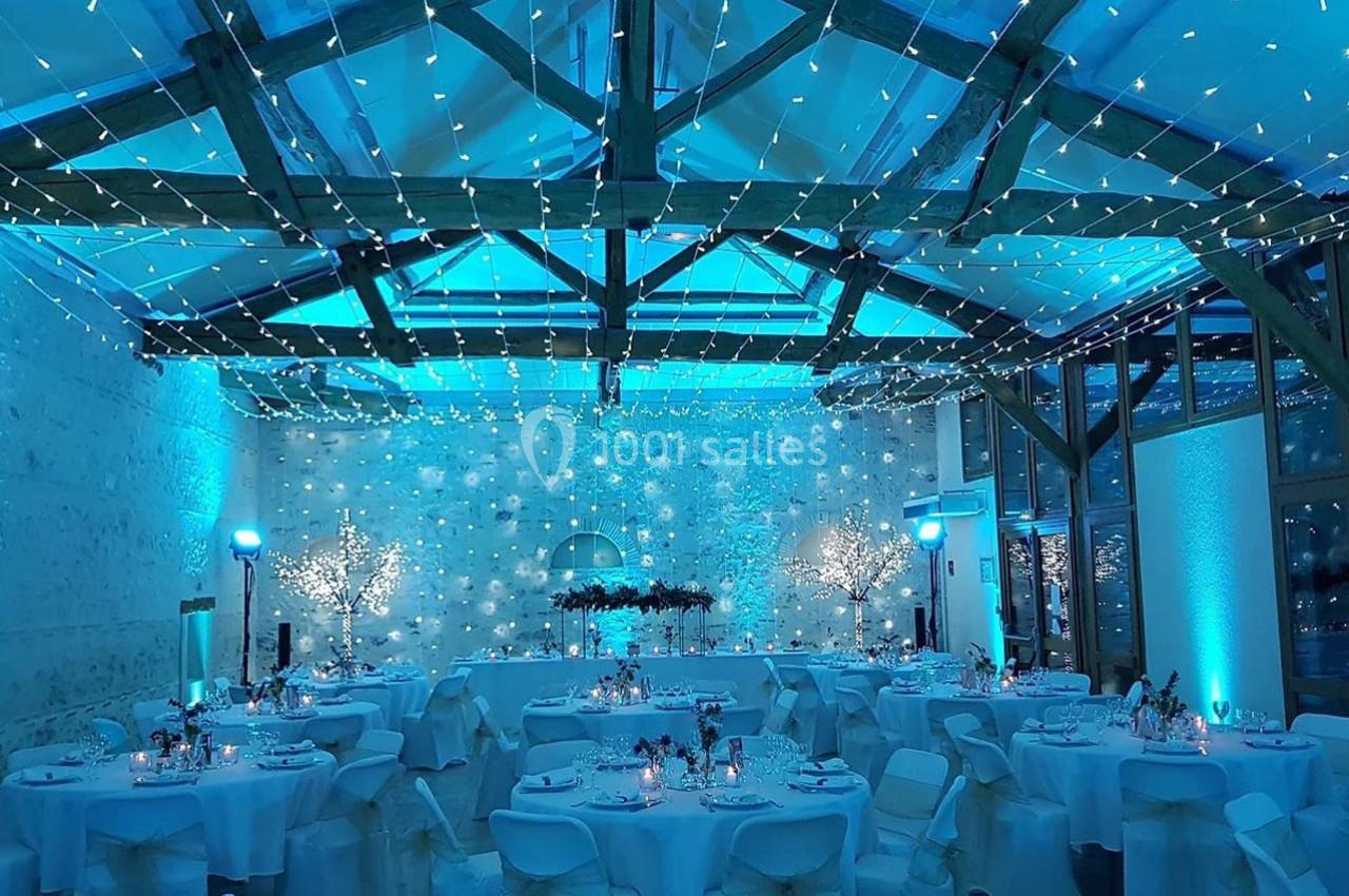 Salle de réception décorée avec des guirlandes lumineuses, tables dressées et ambiance lumineuse bleutée.