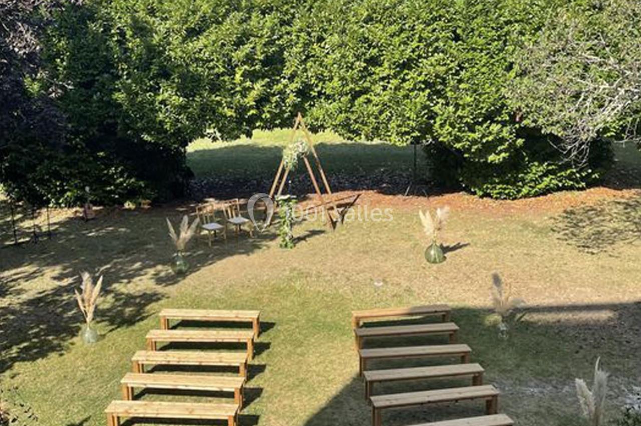 Disposition de bancs en bois face à une arche décorée pour une cérémonie en plein air, entourée de verdure.