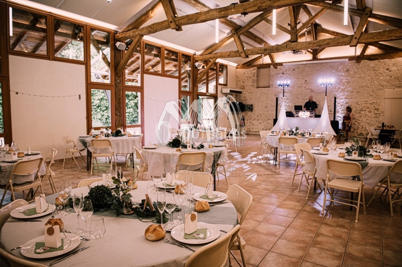Salle de réception décorée pour un mariage, avec tables rondes dressées et éclairage tamisé.