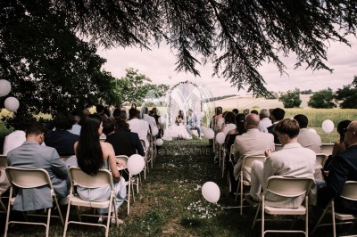 Disposition de bancs en bois face à une arche décorée pour une cérémonie en plein air, entourée de verdure.