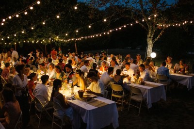Groupe de personnes discutant sous des guirlandes lumineuses dans un jardin en soirée.