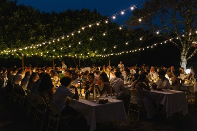 Groupe de personnes discutant sous des guirlandes lumineuses dans un jardin en soirée.
