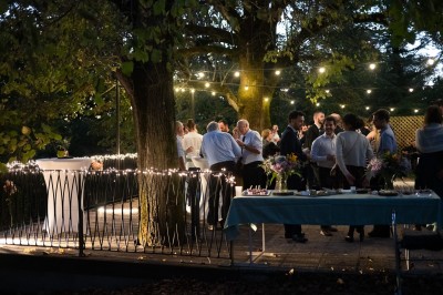 Groupe de personnes discutant sous des guirlandes lumineuses dans un jardin en soirée.