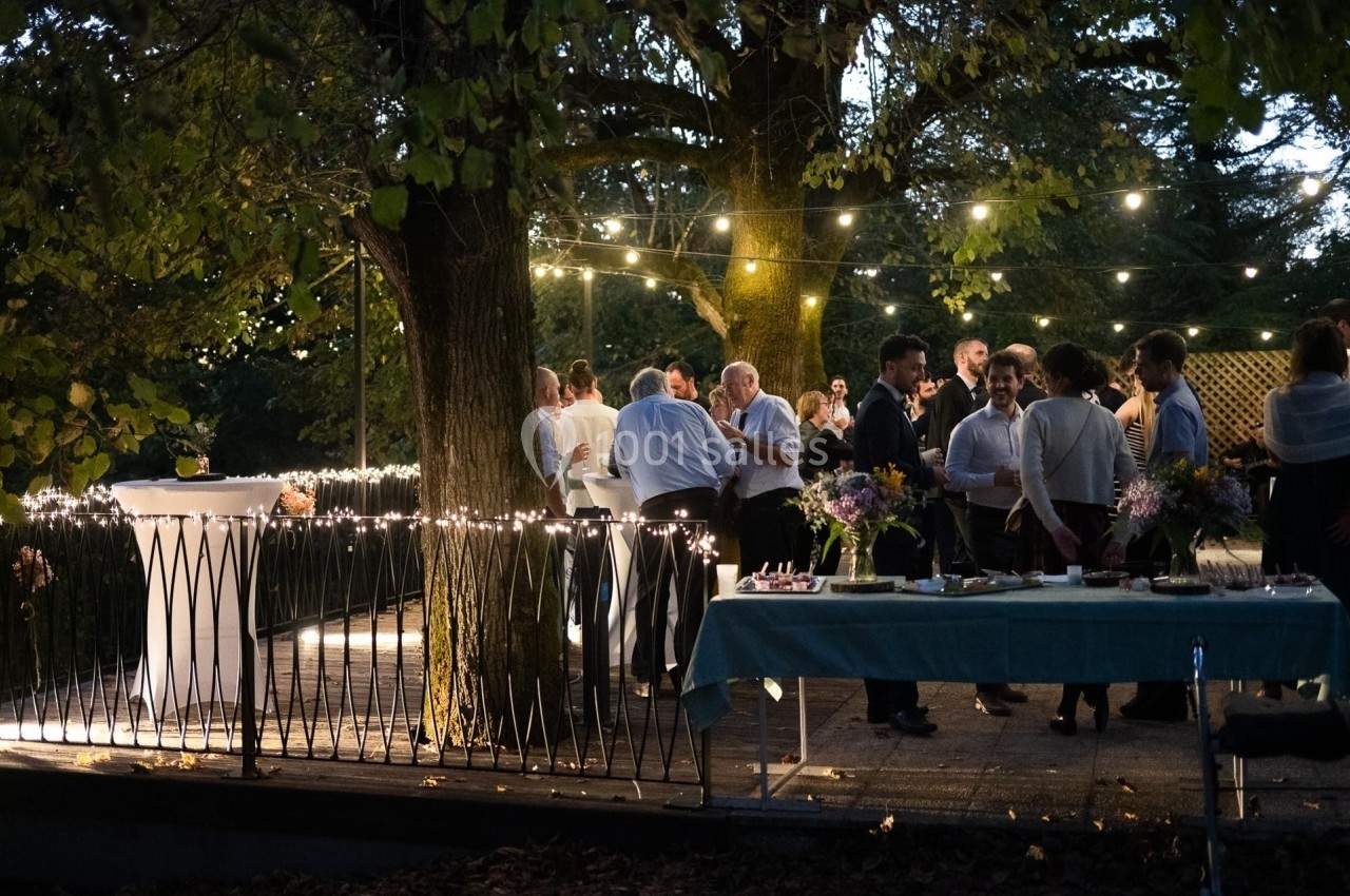 Groupe de personnes discutant sous des guirlandes lumineuses dans un jardin en soirée.