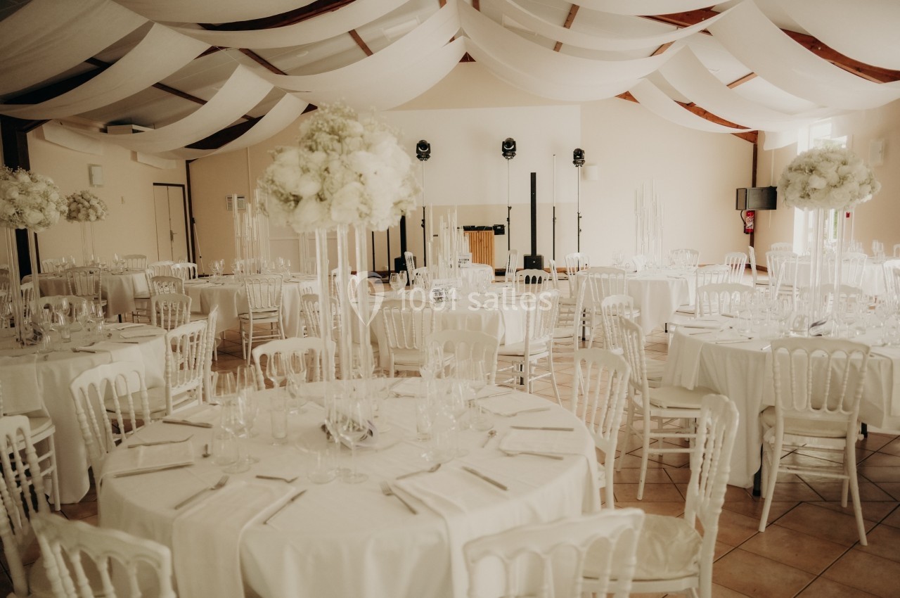 Salle de réception décorée avec des tables rondes, nappes blanches, chaises assorties et arrangements floraux élégants.