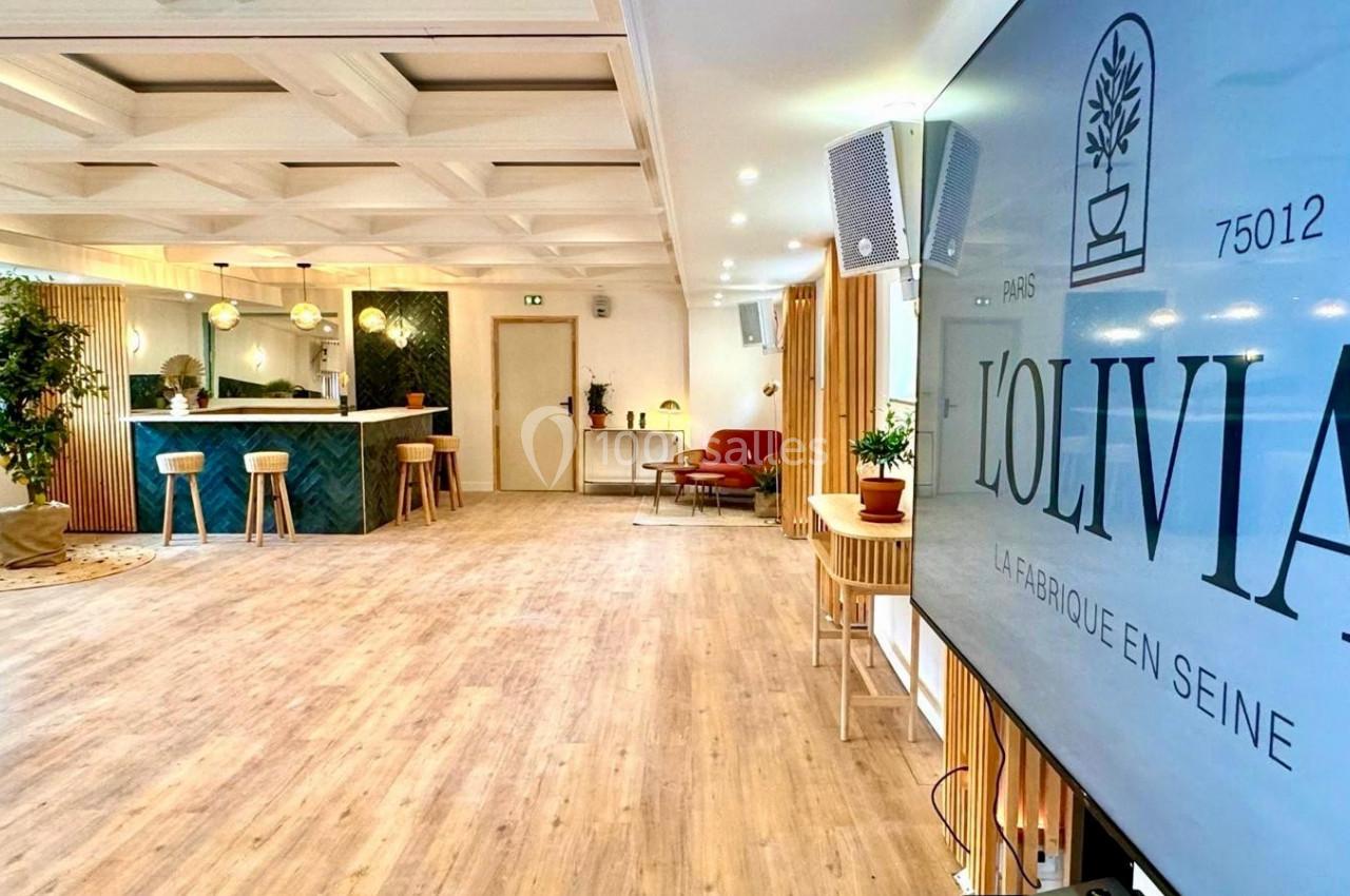Salle lumineuse avec parquet, comptoir moderne, plantes décoratives et écran affichant ’Lolivia, la fabrique en Seine’.