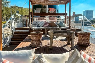 Entrée d'un restaurant aménagé sur un bateau, avec une passerelle en bois et des plantes en pot.