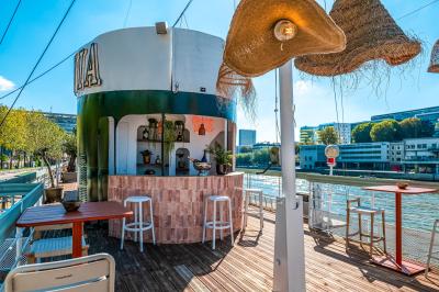 Entrée d'un restaurant aménagé sur un bateau, avec une passerelle en bois et des plantes en pot.