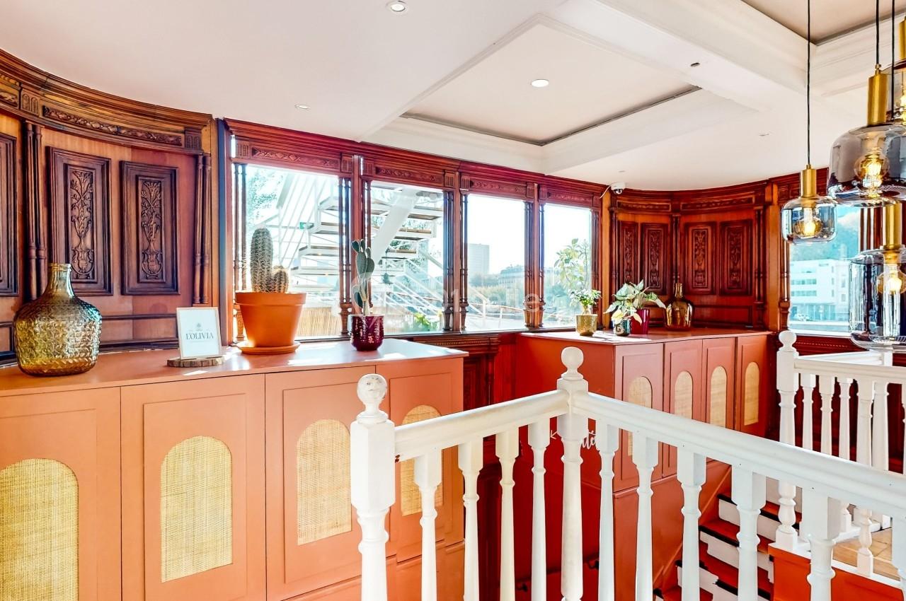 Intérieur lumineux avec boiseries sculptées, plantes, suspensions modernes et vue sur l'extérieur à travers de grandes…