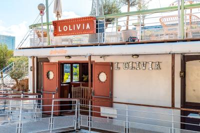 Entrée d'un restaurant aménagé sur un bateau, avec une passerelle en bois et des plantes en pot.