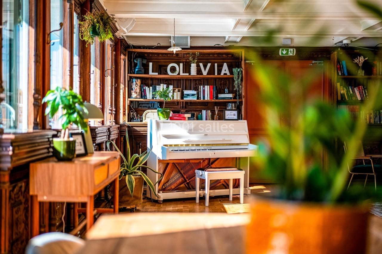 Piano blanc dans une pièce lumineuse avec des étagères en bois, des plantes et une décoration chaleureuse.