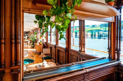 Entrée d'un restaurant aménagé sur un bateau, avec une passerelle en bois et des plantes en pot.