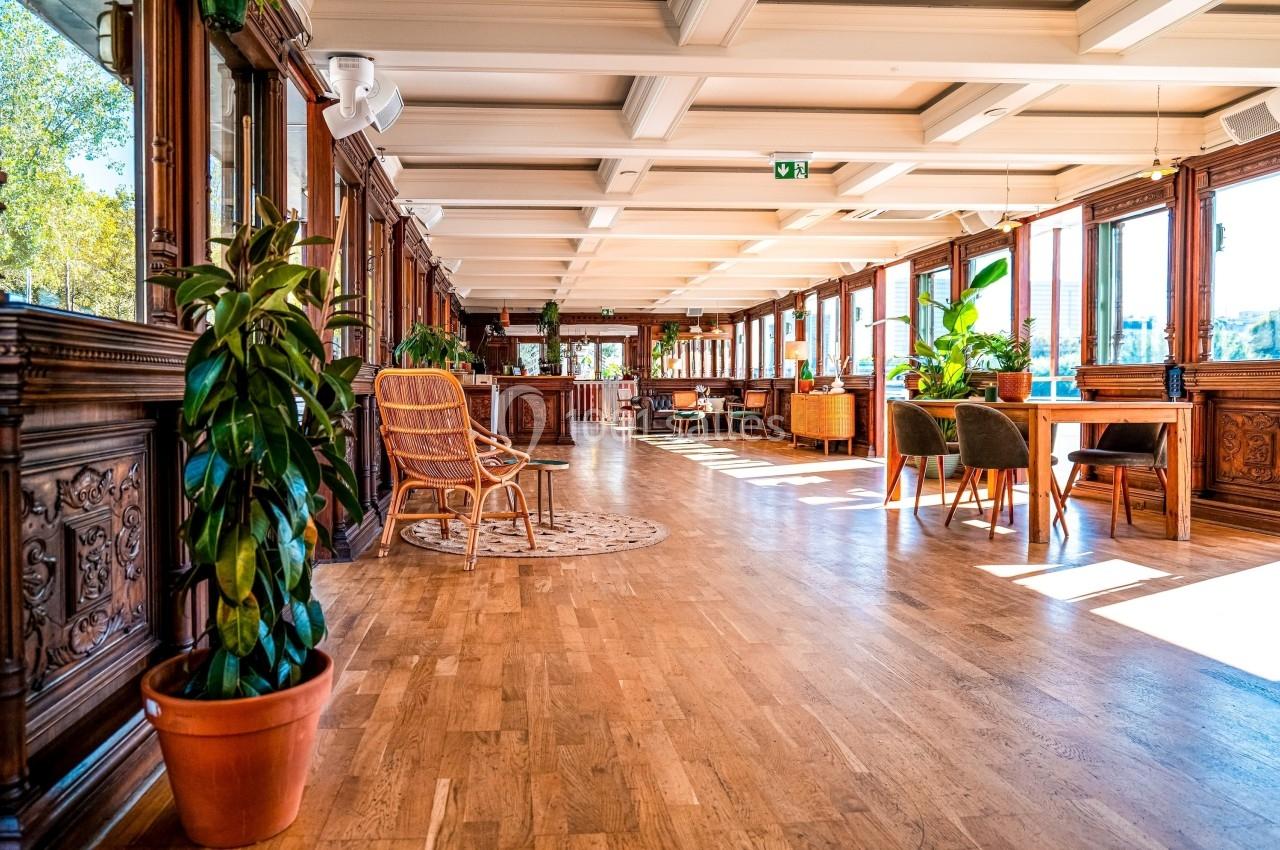 Intérieur lumineux avec parquet, grandes fenêtres, plantes en pot et mobilier en bois dans un espace ouvert.