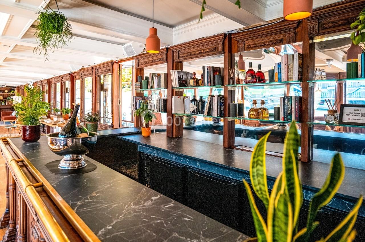 Intérieur d'un bar avec comptoir en marbre, étagères en bois garnies de bouteilles et plantes décoratives.