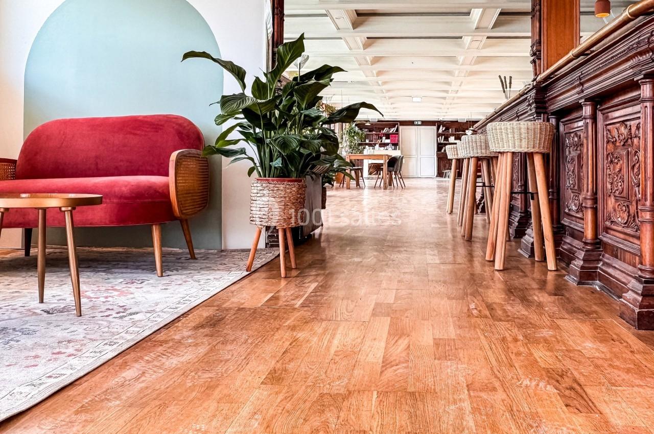 Espace intérieur lumineux avec parquet, canapé rouge, plantes en pot et comptoir en bois sculpté.