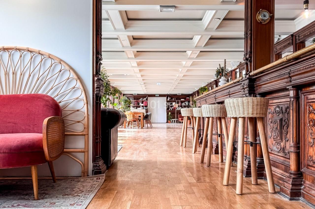 Espace intérieur lumineux avec un bar en bois sculpté, des tabourets en rotin et un fauteuil rouge près d'une cloison.